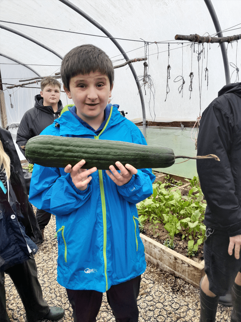Learner from The Stable School holding a luffa vegetable during a hands-on activity at Magdalen Farm.